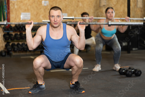 Middle-aged male bodybuilder performing strength and endurance exercises during group barbell lifting in CrossFit class