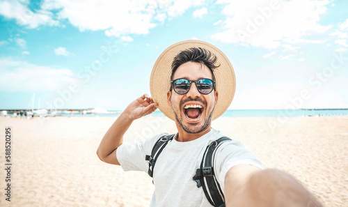 Handsome young man taking selfie picture at beach summer vacation - Smiling guy having fun walking outside - Summertime holidays and technology concept