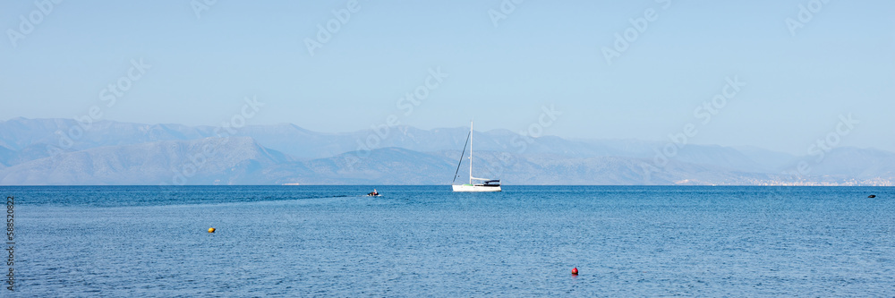 Fantastic seaside view at the sea with the alone yacht on the horizon, Corfu island, Greece. Sunny day, minimalism, calm and silence.