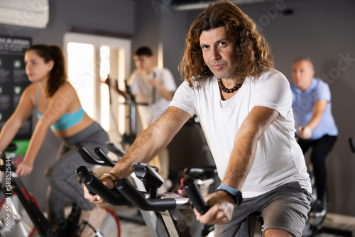Focused sporty adult man working out on stationary bicycle in gym. Physical activity and fitness concept