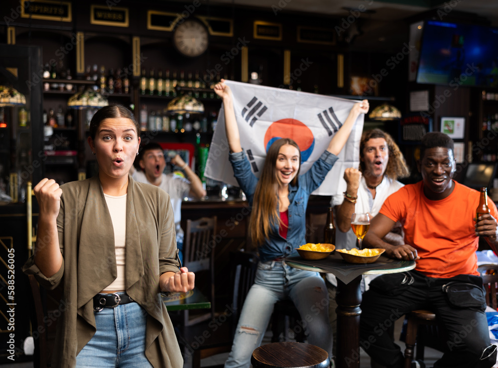 Excited young woman, South Korea football team fan spending time in bar with friends. People with state flag in pub.