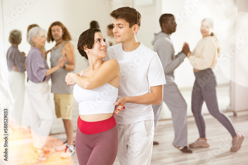 Smiling young Hispanic woman and handsome guy attending group choreography class, learning modern dynamic pair dances. Concept of active lifestyle..