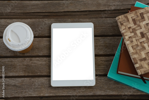 Disposable glass, books and digital tablet on wooden plank