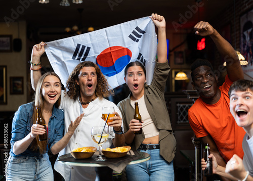 Diverse men and women supporting South Korea sports team in pub together. Happy group of friends raising German flag.
