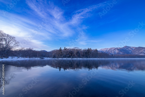 湖畔の森の木々と山と空を水面に反射する湖。日本の北海道の屈斜路湖。
