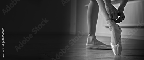 Ballerina tying pointe shoes in dance studio, closeup. Black and white effect. Banner design with space for text