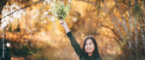Dreamy beautiful girl with thistle flowers on bokeh background with yellow leaves. White fluff in golden sunlight. Inspired girl in autumn forest. Female beauty portrait among flying spores of thistle