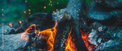 Vivid smoldered firewoods burned in fire close-up. Atmospheric background with orange flame of campfire. Full frame image of bonfire. Warm whirlwind of glowing embers and ashes in air. Sparks in bokeh