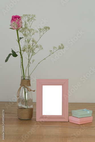 Rose flower in glass vase, photo frame and gift boxes on a table