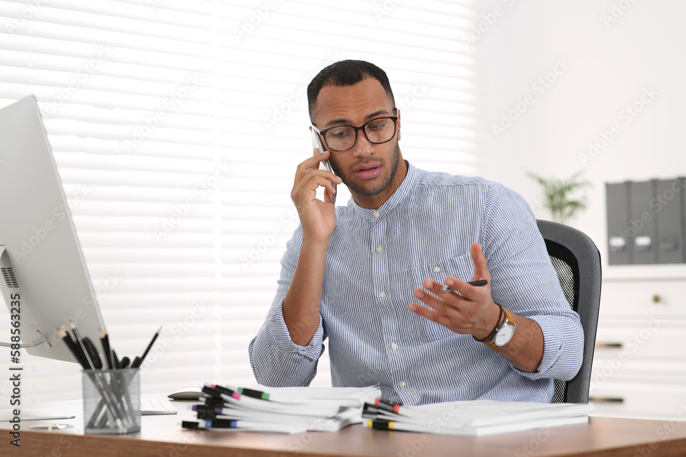 Man talking on phone while working with documents at wooden table in office Man talking on phone while working with documents at wooden table in office