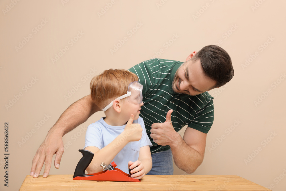 Fototapeta premium Father with son showing thumbs up and plane at table near beige wall. Repair work