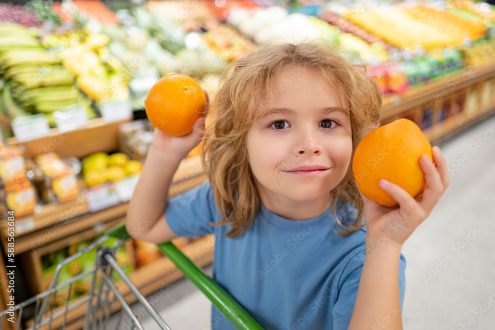 Fototapeta premium Portrait of child with shopping basket purchasing food in grocery store. Funny kids face. Sales and shopping. Kid buying products at supermarket. Supermarket and grocery shop. Discount, sale concept.