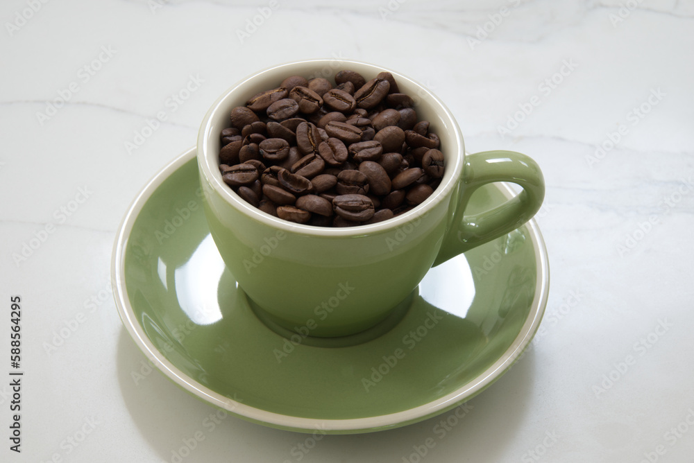 Medium sized green coffee cup filled with whole roasted coffee beans Medium sized green coffee cup filled with whole roasted coffee beans