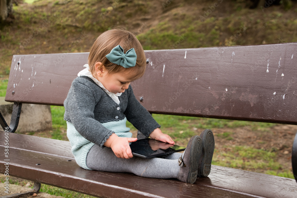 2 year old girl playing in the park with the tablet instead of non-virtual games.