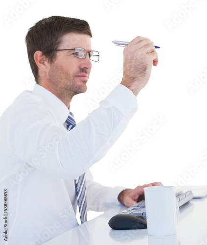Businessman holding pen up at desk