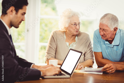 Businessman using laptop while sitting with senior people
