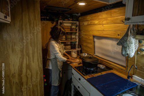 Senior woman prepares flatbreads in the kitchen of a motorhome at night.
