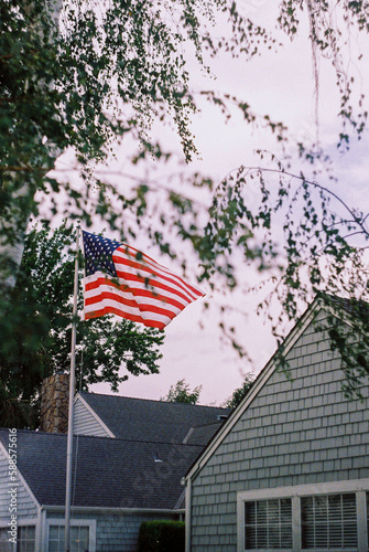 American flag waving with the wind on a suburbian porch with a tree infront photo