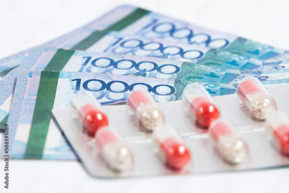 © Roman - Blister with pills drug on top of stack of Tenge Kazakhstan money bills on white background.