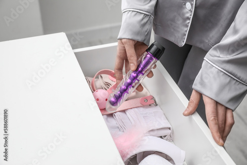Woman taking vibrator from open drawer in bedroom, closeup