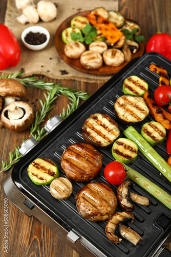 Modern electric grill with tasty vegetables on wooden background