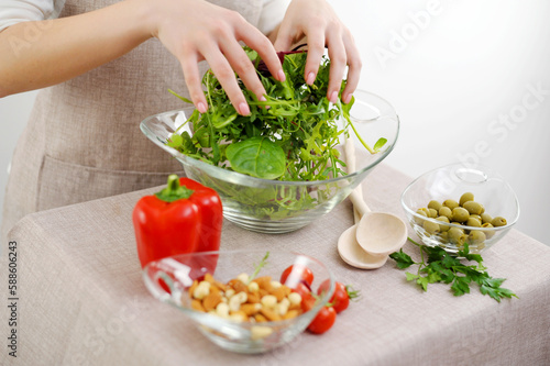 girl is stirs freshly prepared salad from arugula, cherry tomatoes, and mozzarella with your hands in a wooden bowl, around the ingredients are laid out top view. High quality photo