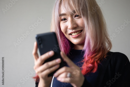 Portrait of beautiful Asian stylish trendy girl model using smartphone in casual summer clothes. pastel pink and red hair