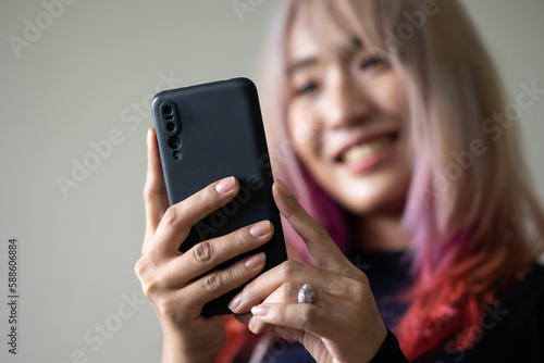 Portrait of beautiful Asian stylish trendy girl model using smartphone in casual summer clothes. pastel pink and red hair