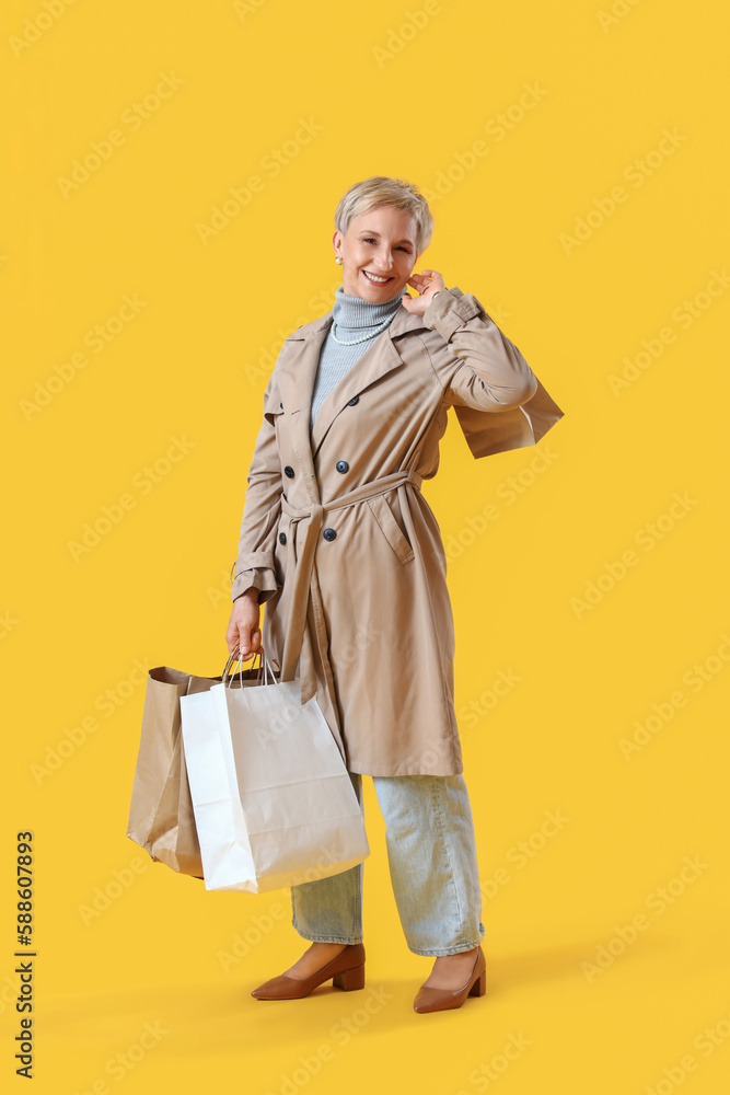 Beautiful mature woman with shopping bags on yellow background Beautiful mature woman with shopping bags on yellow background