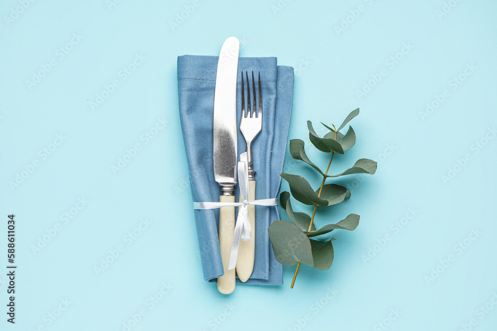 Set of cutlery in napkin and eucalyptus branch on blue background Set of cutlery in napkin and eucalyptus branch on blue background