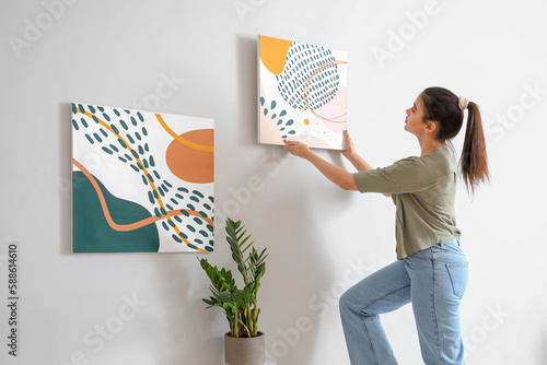 Fotografie Young woman hanging picture on wall in living room
