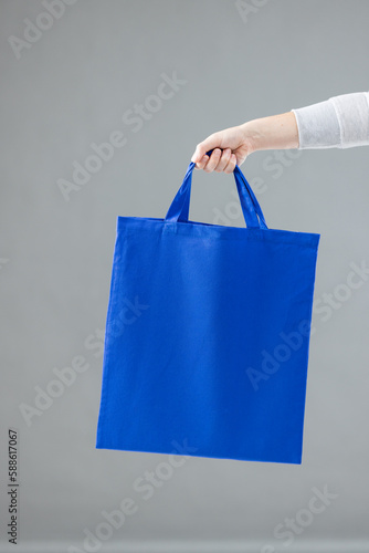 Hand of caucasian woman holding blue canvas bag with copy space on grey background