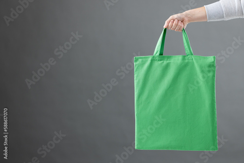Hand of caucasian woman holding green canvas bag with copy space on grey background