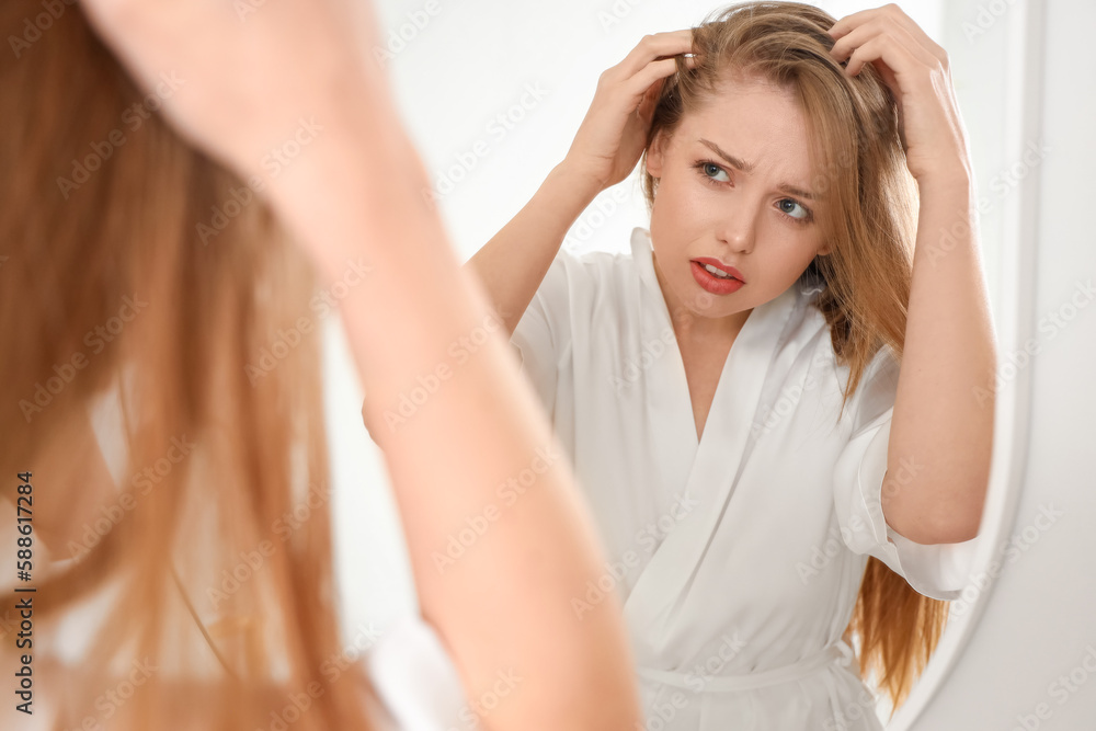 Worried young woman with hair loss problem looking in mirror at home Worried young woman with hair loss problem looking in mirror at home