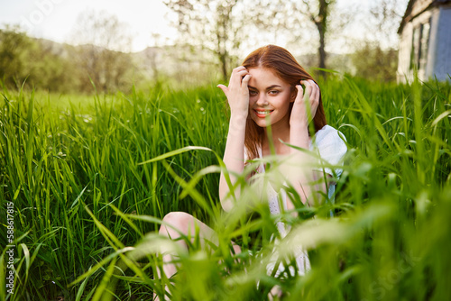 a young woman sitting resting in the tall grass straightening her hair