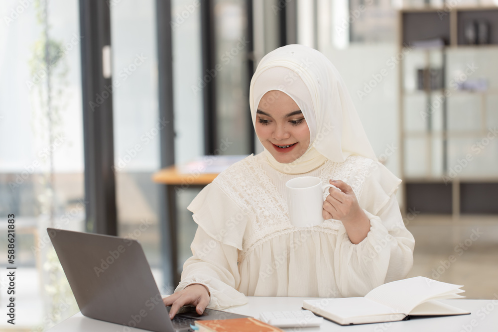 Happy Asian Muslim Woman working at desk in office, Businesswoman and education online concept. Happy Asian Muslim Woman working at desk in office, Businesswoman and education online concept.