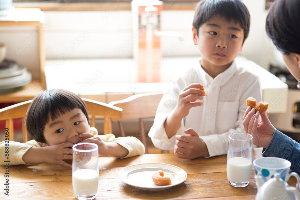 キッチンのテーブルでドーナツを食べる兄弟と母親