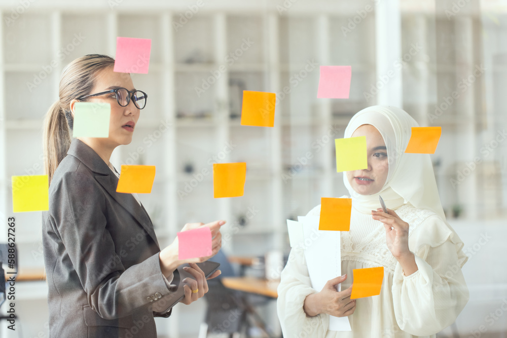 Asian woman team working on project plan using sticky papers notes on glass wall, people meeting to share idea, Business design planning concepts.