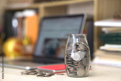 The glass bottle filled with coins is next to the computer