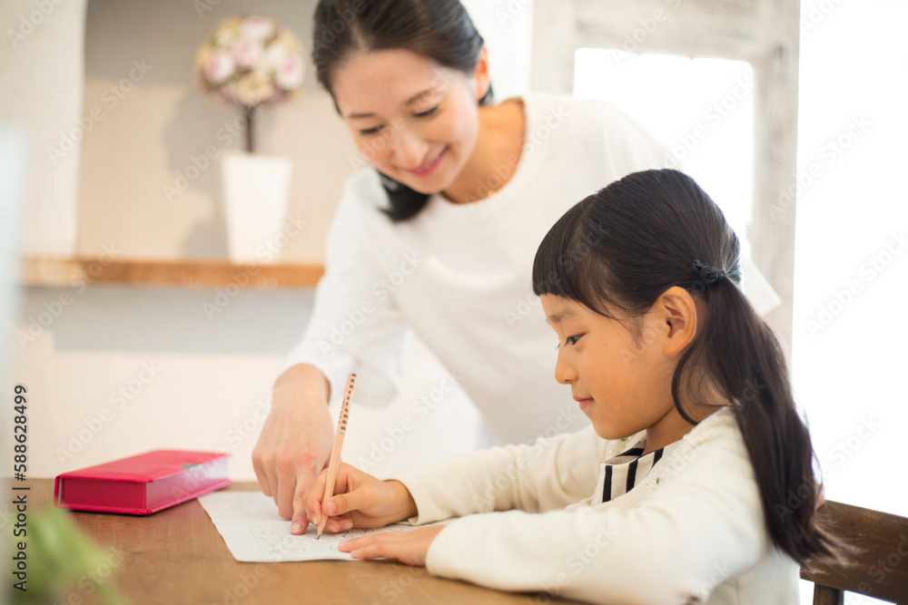 机に向かって勉強する女の子とノートを指さす母親 机に向かって勉強する女の子とノートを指さす母親