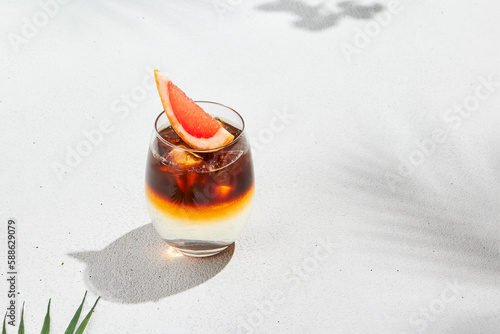 Trendy summer drink - espresso tonic on white background with shadow of sun. Cold coffee cocktail in summer sunny day. Coffee menu. Aesthetic composition with iced espresso and tonic cocktail.