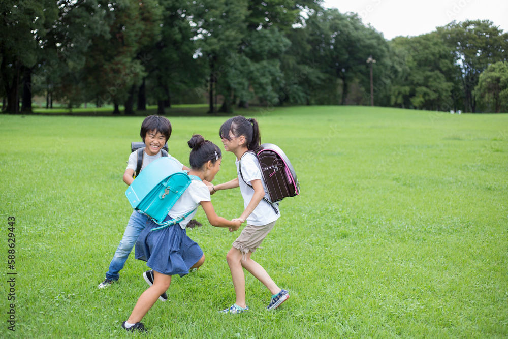 草原で手を繋いで遊ぶランドセルを背負った小学生達