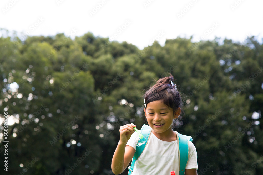 シャボン玉を飛ばして遊ぶランドセルを背負った小学生の女の子