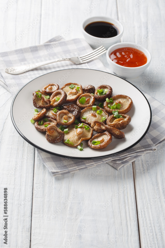 Fried shiitake mushrooms close-up on a plate served with chili and soy sauces on a wooden table. Vertical Fried shiitake mushrooms close-up on a plate served with chili and soy sauces on a wooden table. Vertical