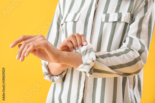 Young woman rolling up her sleeve on yellow  background, closeup