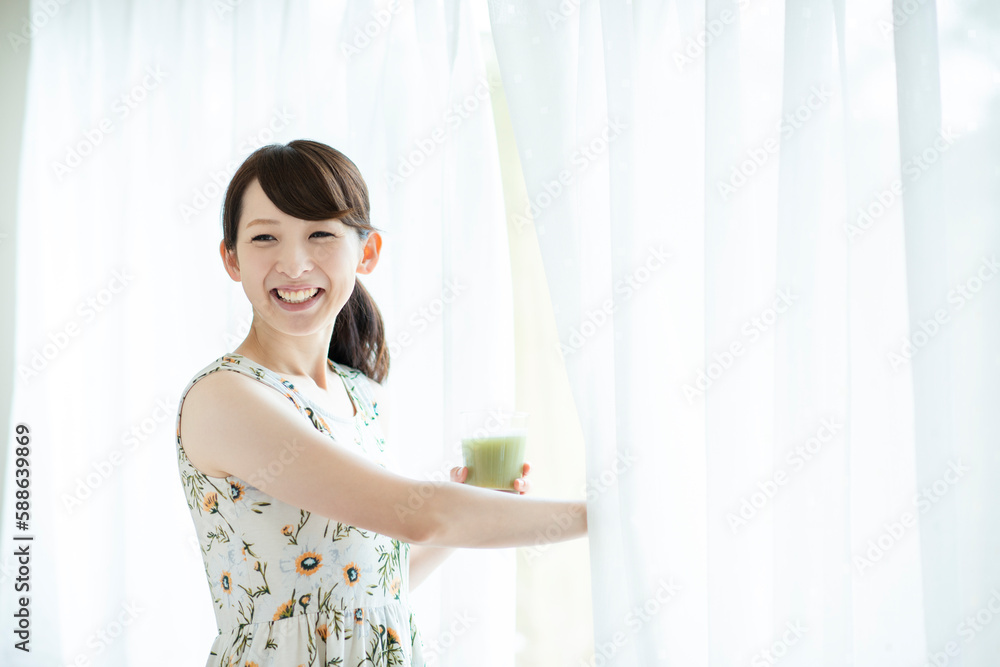 スムージーを持ちカーテンを開ける女性 スムージーを持ちカーテンを開ける女性