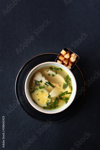 Fresh fish soup with croutons in a bowl on a black background, top view. White fish soup. Transparent broth. A healthy dish. Lean menu.Vertical photo.Space for copying.He was lying flat.