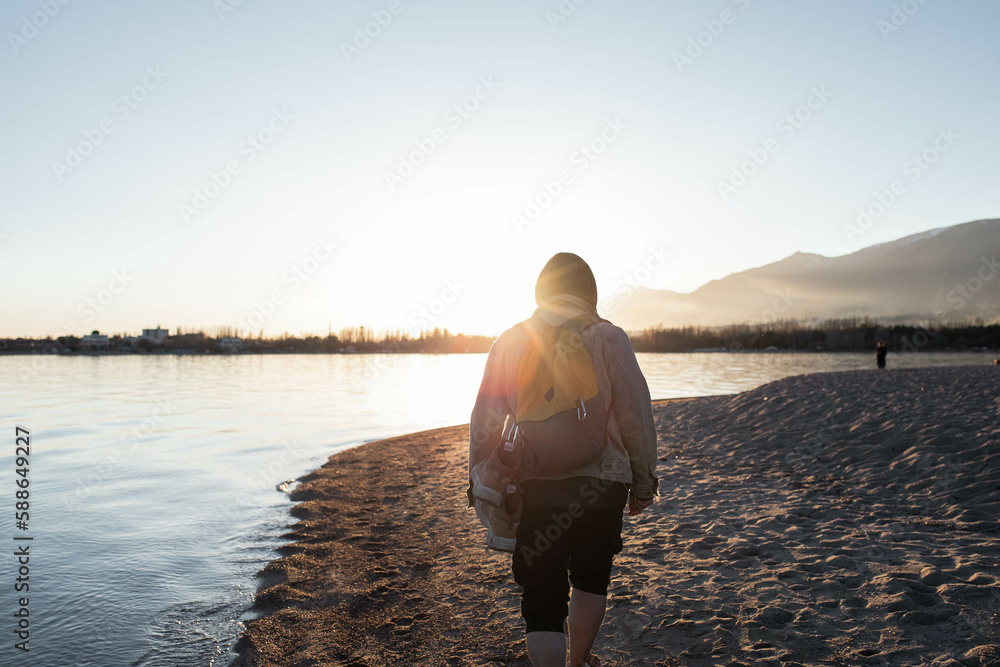 Man Walking Along Lake Shore at Sunset with Mountains 
