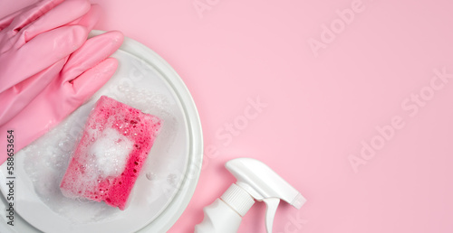 Detergent, soapy kitchen sponge and clean plates on a pink background. Close-up. Copy space. Top view. Selective focus.
