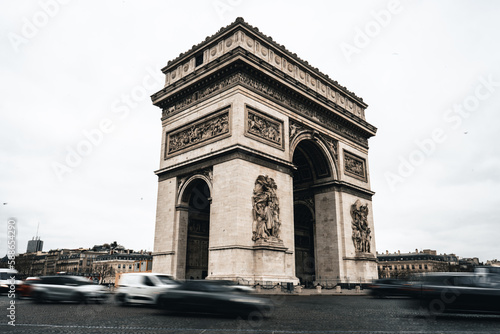 Fototapeta Naklejka Na Ścianę i Meble -  Arc de Triomphe mit Autos im Vordergrund welche in Bewegung sind und hellem bewölkten Himmel